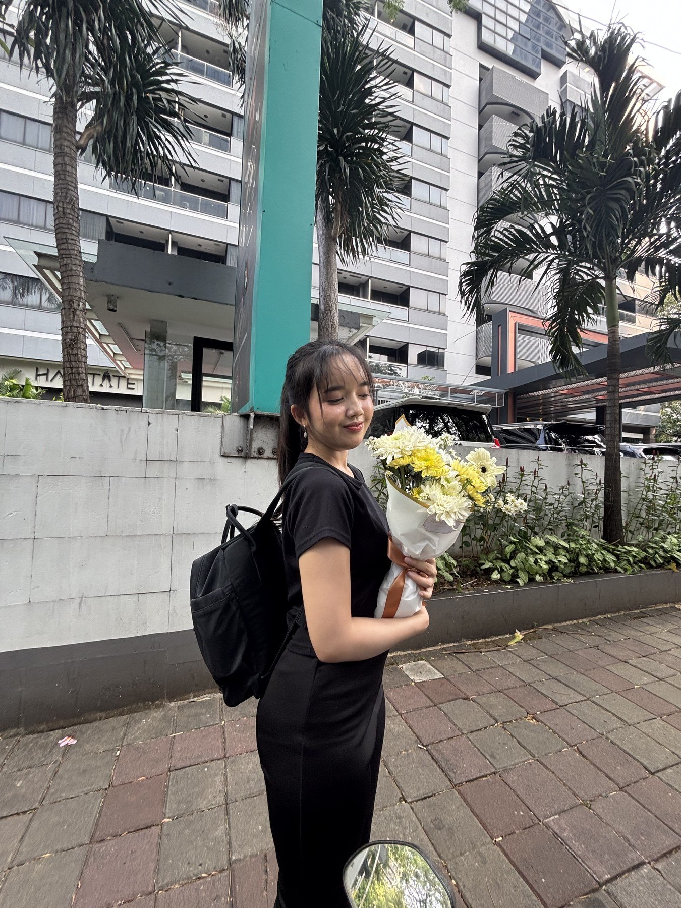 Dea membawa buket bunga putih di depan gedung
