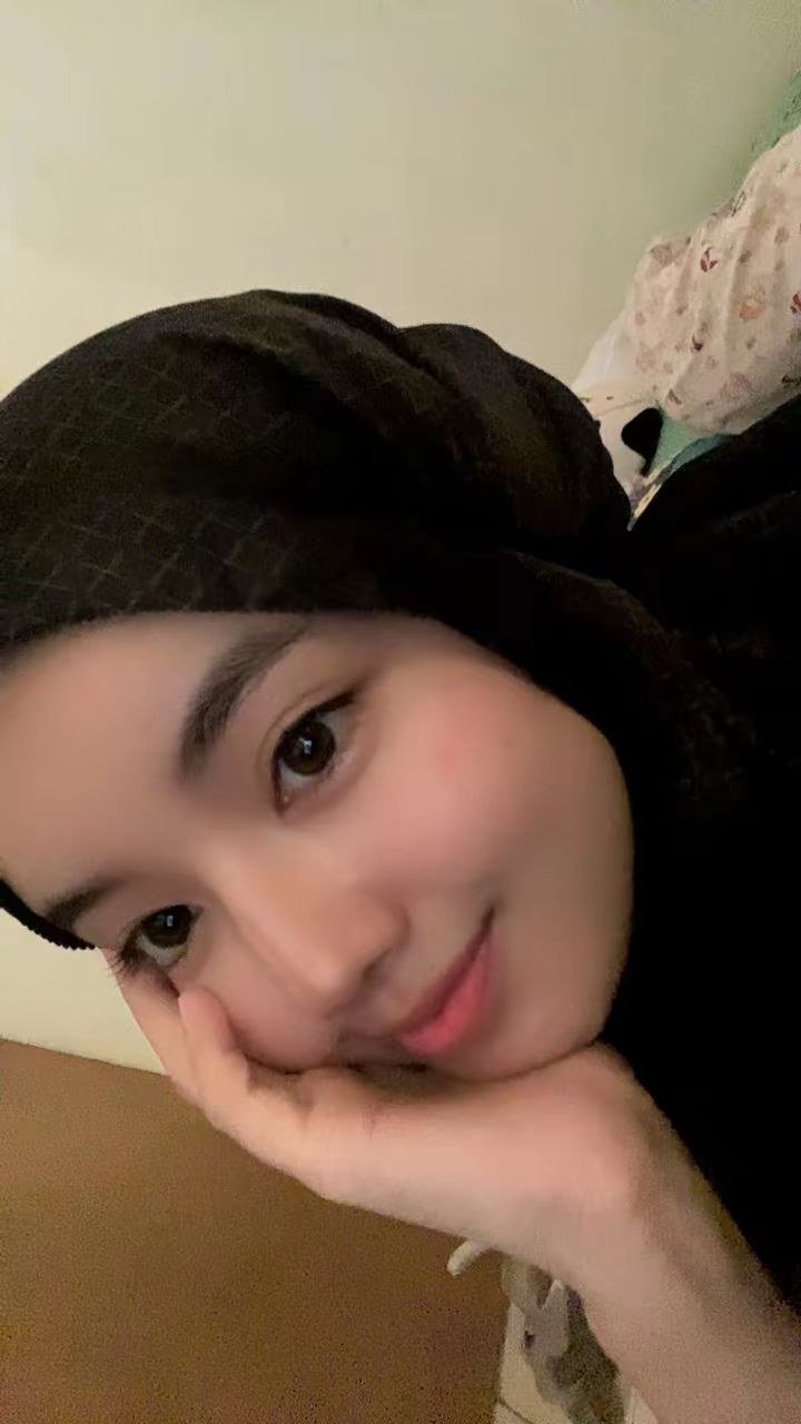 Dea berhijab hitam, tersenyum sambil menyandarkan wajah di tangan